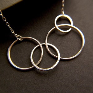 May include: A silver necklace featuring four interlocking circles. The circles are of varying sizes and are attached to a silver chain.