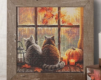 May include: Cross-stitch artwork in a rustic wooden frame. The image depicts two cats gazing out a window at an autumn scene with a pumpkin, candles, and fall foliage. The color palette includes shades of brown, orange, and gray.