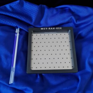 May include: A black tray with a grid of small holes and the text "MEY-RAH-KEE" on the top. The tray is sitting on a blue surface.