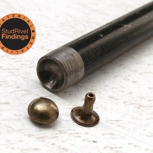 May include: A close-up of a metal tool for setting rivets. The tool is black and has a round head. There are two brass rivets, one with a round head and one with a post. The tool is labelled "Material Metal Iron StudRivet Findings".