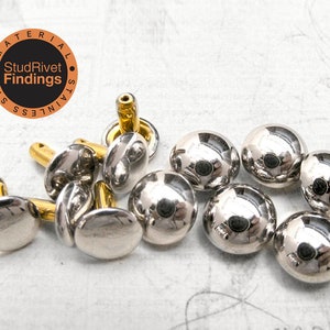 Puede incluir: Un conjunto de tachuelas met&aacute;licas plateadas brillantes con tapas redondeadas y postes dorados. Las tachuelas est&aacute;n dispersas sobre una superficie clara. La imagen incluye un logotipo circular con el texto "StudRivet Findings".