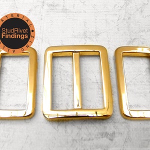 May include: Three gold-toned metal belt buckle slides. The buckles are rectangular with rounded corners and have a smooth, polished finish.
