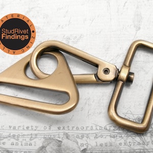 May include: A gold-toned metal triangle swivel hook with a rectangular loop. The hook is attached to a metal D-ring. The hook is made of zinc alloy.