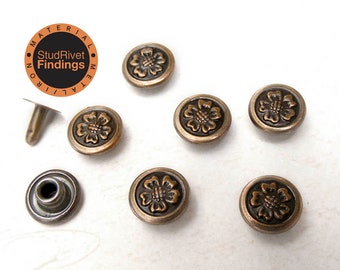Op de afbeelding: Zes antieke messingkleurige bloemvormige klinknagels met een reliëfdesign. De klinknagels hebben een diameter van 1,25 cm en worden geleverd met twee sets pennen en doppen.