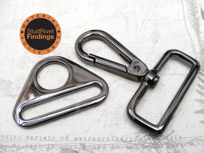 May include: Two black metal hardware pieces for bags or other crafts. The piece on the left is a triangle-shaped D-ring with a round opening. The piece on the right is a rectangular swivel hook with a spring-loaded clasp.