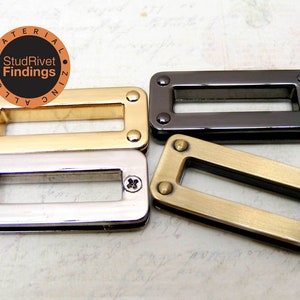 May include: Four rectangular metal findings in gold, silver, gunmetal, and antique brass finishes. Each has rounded corners and is secured with small rivets. The text "StudRivets Findings" is in a circular logo.