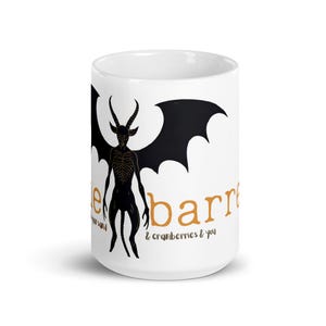 May include: A white ceramic mug featuring a black graphic of a winged, horned creature with a skeletal chest. The text "the barrel & cranberries & you" is printed in orange and black lettering across the front of the mug, partially obscured.