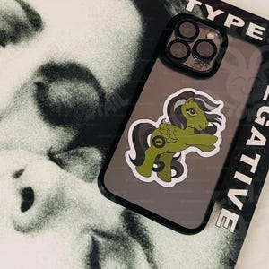 Może przedstawiać: Czarne etui na telefon z zielono-białą naklejką My Little Pony z tyłu. Etui ma czarną ramkę, a na boku nadrukowano napis "TYPE NEGATIVE".