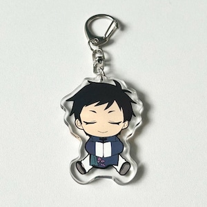 May include: A clear acrylic keychain featuring a cartoon character with black hair, wearing a blue and purple outfit. The character has closed eyes and a relaxed expression.
