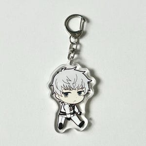 May include: A clear acrylic keychain featuring a cartoon character with white hair, wearing a white shirt and black pants. The character has blue eyes and a serious expression.
