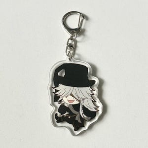 May include: A black and white anime character keychain with a white hat and long white hair. The character is smiling and wearing a black outfit. The keychain is attached to a silver metal ring.