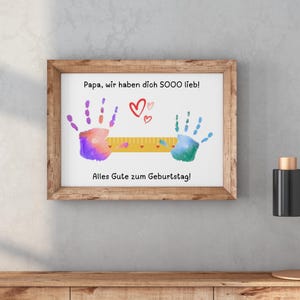 May include: A framed print with a wooden frame. The print features colorful handprints, hearts, and German text. The text reads "Papa, wir haben dich SOOO lieb!" and "Alles Gute zum Geburtstag!"