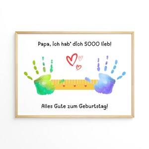 May include: A framed print with the text "Papa, ich hab' dich SOOO lieb!" and "Alles Gute zum Geburtstag!" features colorful handprints and hearts. A yellow ruler is between the handprints. The print is in a light wood frame.