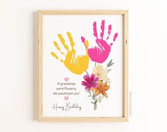 May include: A framed print with a light wood frame. The print features two handprints, one yellow and one pink, with a bouquet of flowers. Text reads "If grandmas were flowers, we would pick you! Happy Birthday."