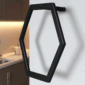 May include: A black, hexagonal towel ring fixed to a white wall. The geometric design has a matte finish, offering a modern touch to a bathroom or kitchen. The towel ring is a stylish, space-saving accessory.