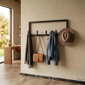 Può includere: Un appendiabiti da parete rettangolare in metallo nero con cinque ganci. Supporta una sciarpa grigia, una borsa a tracolla in pelle color cuoio, una giacca di jeans blu e un cappello in feltro marrone a tesa larga come soluzione di archiviazione.