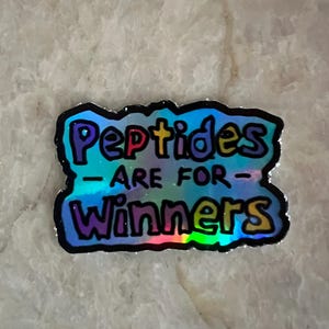 Könnte beinhalten: Ein holografischer Aufkleber mit den Worten "Peptides ARE FOR Winners" in bunten Buchstaben. Der Aufkleber hat einen schwarzen Rand und ein glänzendes, irisierendes Finish, das verschiedene Farben reflektiert.