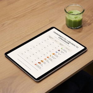 May include: A digital tablet displaying a Fahrenheit to Celsius conversion chart, with food icons. A glass of green liquid sits nearby on a wooden table. The chart includes the text "FAHRENHEIT (&deg;F) &rarr; CELSIUS (&deg;C) CONVERSION".
