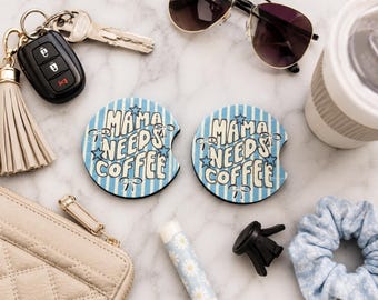 May include: Two blue and white striped car coasters with the text "MAMA NEEDS COFFEE" in a retro font. The coasters are surrounded by keys, sunglasses, a coffee cup, a purse, and other accessories.