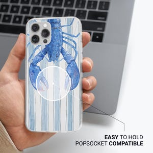 K&ouml;nnte beinhalten: Transparente Handyh&uuml;lle mit einem blauen Aquarell-Hummer-Design auf gestreiftem Hintergrund. Auf der H&uuml;lle steht "EASY TO HOLD POPSOCKET COMPATIBLE". Die Handyh&uuml;lle wird von einer Person in der Hand gehalten.