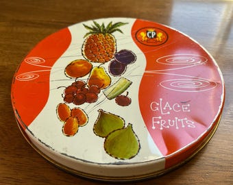 May include: Round metal tin with a white and red design, featuring illustrations of various fruits like pineapple, plums, and figs. The text "GLACE FRUITS" is visible on the side. The tin has a gold rim and a "CP" logo.