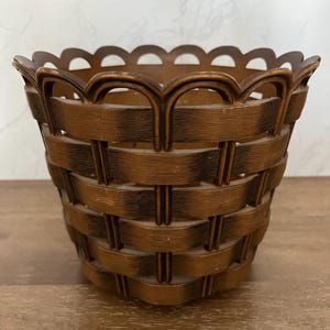 May include: A brown woven basket with a scalloped rim. The basket has a classic, textured design, with a dark brown color. The basket is likely made of plastic or a similar material. The basket is empty.
