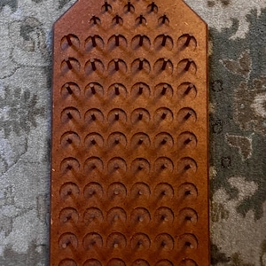 May include: A rectangular brown wooden board with a pointed top, featuring a grid of circular indentations and vertical pegs arranged in rows. The board has a textured, composite material surface with a uniform brown finish throughout the structure.