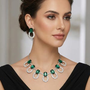 Può includere: Elegante parure di gioielli con collana e orecchini abbinati. La collana e gli orecchini presentano pietre preziose verdi taglio smeraldo circondate da un alone di cristalli trasparenti scintillanti. I gioielli sono su sfondo scuro.