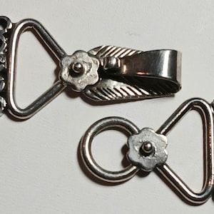 May include: Two silver-toned necklace clasps. Each clasp features a flower design and a series of small loops for attachment. One clasp has a leaf design. The clasps are designed to connect jewelry pieces.