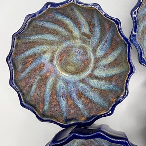 May include: Set of four blue ceramic bowls with a scalloped rim. The bowls have a swirling, iridescent glaze in shades of blue, green, and brown.