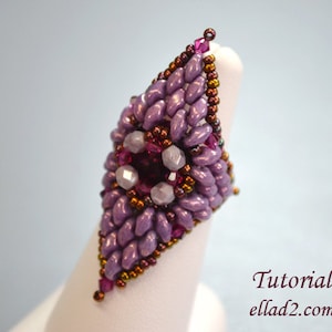 May include: A purple and brown beaded ring with a flower design in the center. The ring is on a white display stand. Tutorial ellad2.com