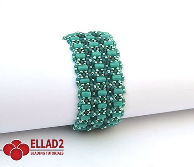 Op de afbeelding: Een turquoise en zilveren kralenarmband met een geweven patroon. De armband is gemaakt met kleine, ronde kralen en rechthoekige kralen.
