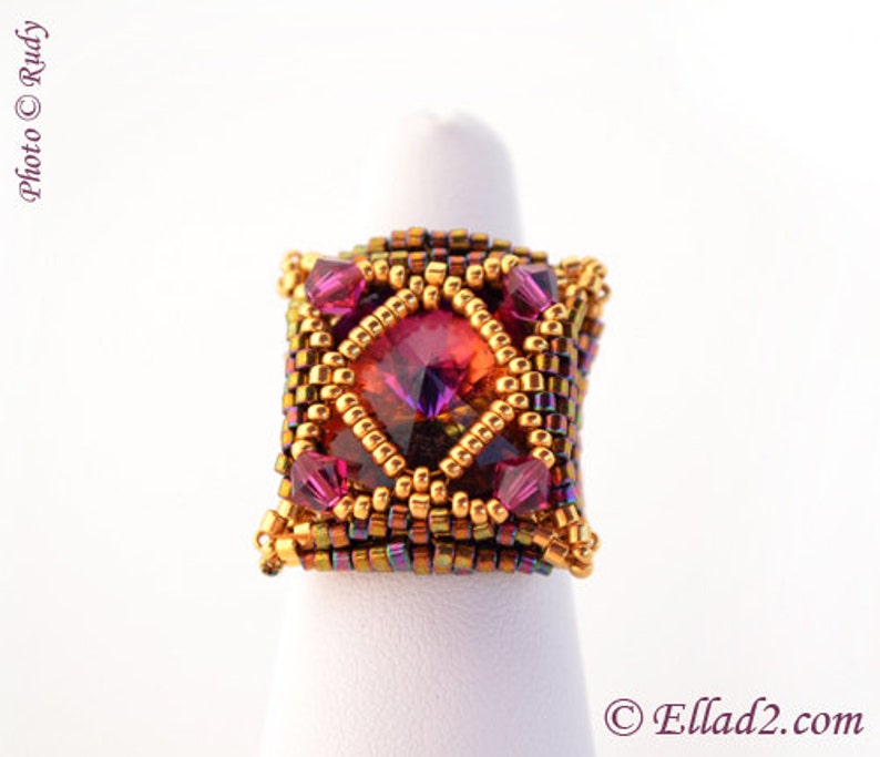 May include: A square-shaped ring with a large, faceted, iridescent purple and orange gemstone surrounded by gold and bronze seed beads.