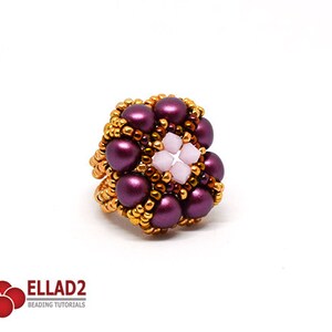 K&ouml;nnte beinhalten: Ein lila-goldener Perlenring mit einem rosafarbenen Zentrum. Der Ring ist aus kleinen Perlen und gr&ouml;&szlig;eren runden Perlen gefertigt.