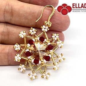 Puede incluir: Pendiente de copo de nieve dorado con un cristal transparente en el centro y cuentas rojas y blancas alrededor. El pendiente cuelga de un gancho dorado.