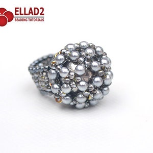 May include: A silver beaded ring with a round, textured design. The ring is made with small, round beads and has a slightly raised center.
