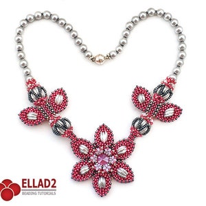 Puede incluir: Un collar de cadena plateada con tres colgantes de flores de cuentas. Las flores son rosas y plateadas con un cristal rosa en el centro de la flor más grande.