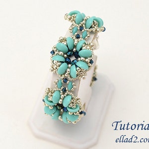 Pode incluir: Um bracelete de contas turquesa e prata com um design floral. O bracelete está em um expositor branco. Tutorial ellad2.com
