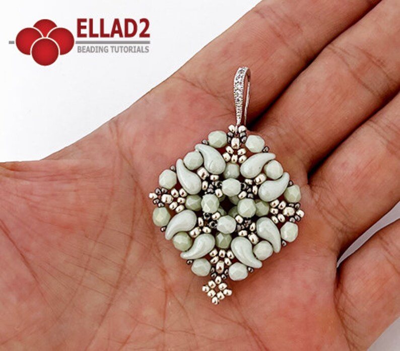 May include: A silver and white beaded pendant with a teardrop shape design. The pendant is hanging from a silver chain.