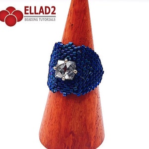 May include: A blue beaded ring with a clear crystal centerpiece. The ring is displayed on a wooden ring stand.  ELLAD2 Beading Tutorials.