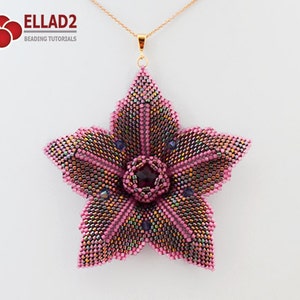 Puede incluir: Un colgante de flor rosa con cuentas con un centro morado oscuro, colgando de una cadena dorada. El colgante tiene forma de estrella de cinco puntas.