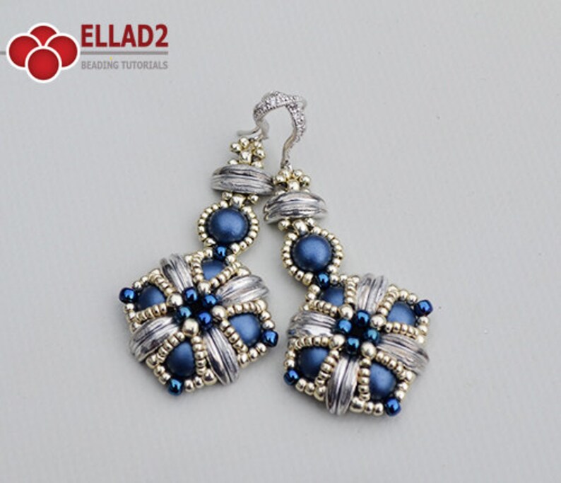 May include: A pair of handcrafted earrings featuring a silver-tone metal design with intricate detailing. The earrings incorporate dark blue beads and small gold-colored accents. The earrings have a square shape with a floral pattern and a decorative top.