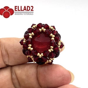 Może przedstawiać: Pierścionek z czerwonym kamieniem szlachetnym, z ozdobnym złotym obramowaniem i skupiskiem czerwonych kryształ&oacute;w wok&oacute;ł kamienia. Pierścionek jest na palcu.