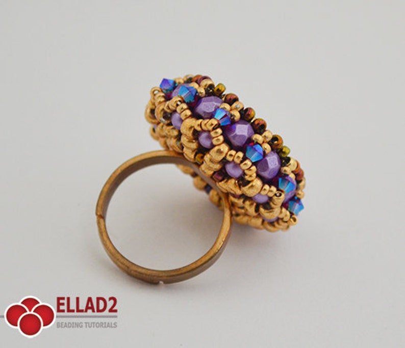 K&ouml;nnte beinhalten: Ein runder Ring aus lila und goldenen Perlen. Der Ring ist aus kleinen Perlen gefertigt und hat eine goldene Band.