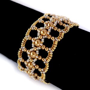 K&ouml;nnte beinhalten: Ein goldfarbenes und wei&szlig;es Armband mit geometrischem Muster. Das Armband ist aus kleinen Perlen und gr&ouml;&szlig;eren runden Perlen gefertigt.