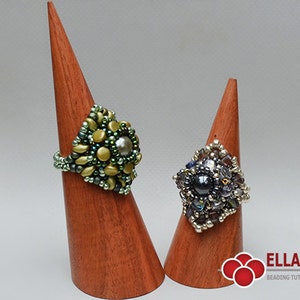 May include: Two beaded rings on wooden display stands. The ring on the left is green and gold with a pearl-like center bead. The ring on the right is silver and black with a dark gray center bead.