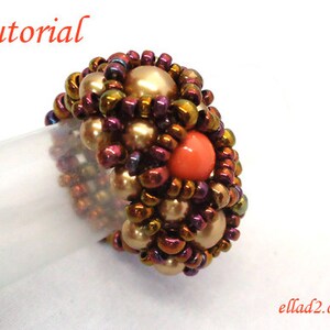 May include: A beaded ring with a large coral-colored bead in the center. The ring is made with small gold and iridescent beads.