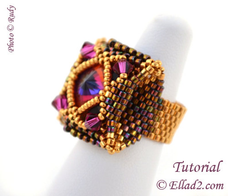 May include: A square-shaped ring with a large, faceted, purple and red gemstone surrounded by gold and iridescent brown seed beads.