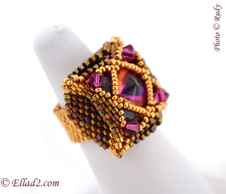May include: A square-shaped ring with a large, faceted, purple gemstone surrounded by smaller, faceted, pink gemstones. The ring is made of gold-colored beads and has a dark brown and gold color scheme.