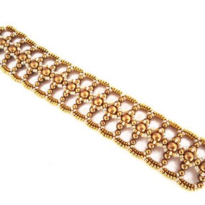 K&ouml;nnte beinhalten: Ein goldfarbenes Armband mit geometrischem Muster. Das Armband besteht aus kleinen goldenen Perlen und wei&szlig;en Perlen.